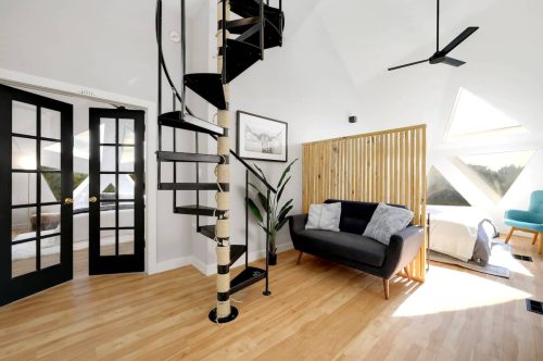 A modern interior featuring a spiral staircase, wooden accents, a sofa, and large windows with natural light.