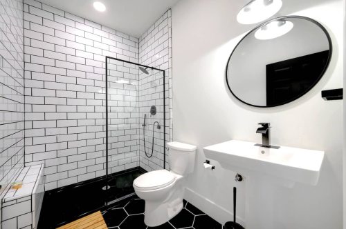 Modern bathroom featuring a glass shower, black and white tile, round mirror, and sleek fixtures.