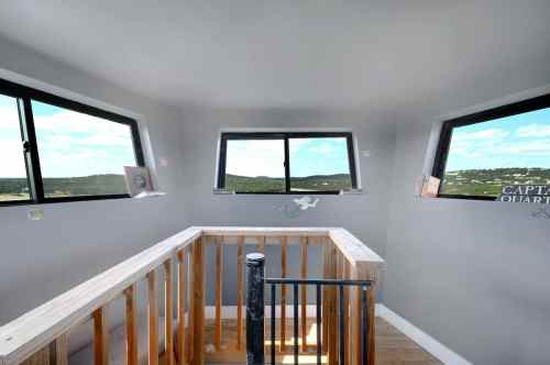 Interior view of a room with large windows, wooden railing, and a scenic landscape visible outside.