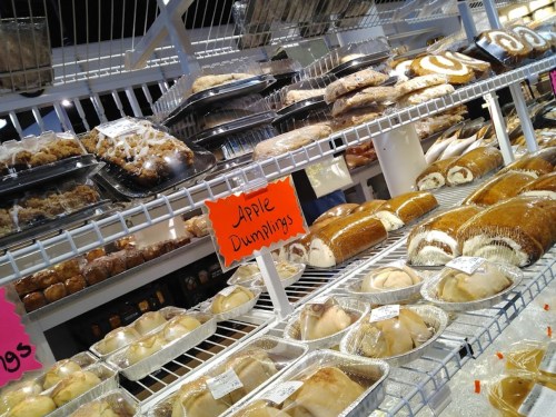 A display of various baked goods, including apple dumplings and rolls, arranged on shelves in a bakery.