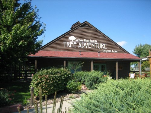 A wooden building with a sign reading "Tree Adventure begins here" at Arbor Day Farm, surrounded by greenery.