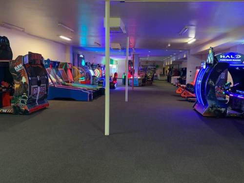 A spacious arcade with various colorful gaming machines and neon lights, featuring both classic and modern games.