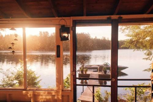 Sunset view from a cabin, showcasing a serene lake and a wooden dock surrounded by trees.