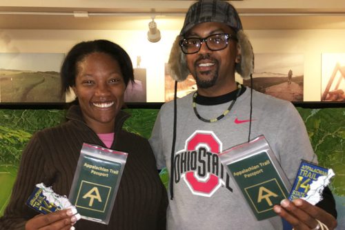 A man and woman hold Appalachian Trail Passports, smiling in front of a nature display.