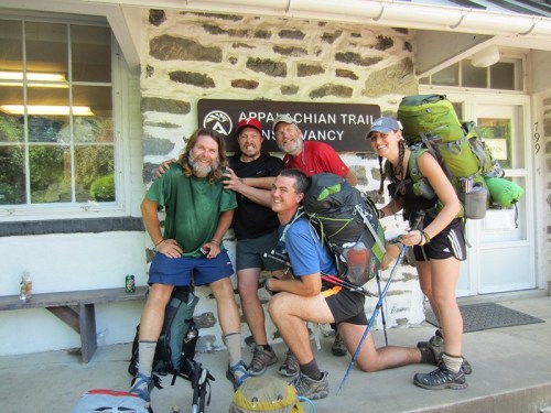 Five hikers pose together outside a stone building, smiling and wearing backpacks, ready for an adventure on the Appalachian Trail.