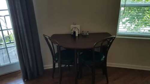 A small dining table with two chairs, set near a window with curtains, in a cozy room.