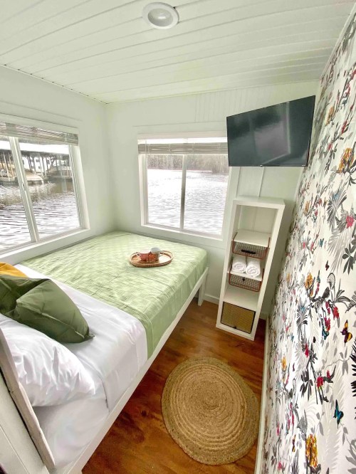 Cozy bedroom with a bed, TV, and large windows overlooking a water view, decorated with floral wallpaper.
