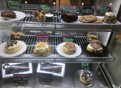 Display case filled with various desserts, including cakes, cupcakes, and cookies, each labeled with colorful signs.