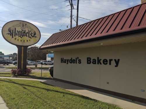 Sign for Haydel's Bakery outside a building with a red roof and green grass in front.