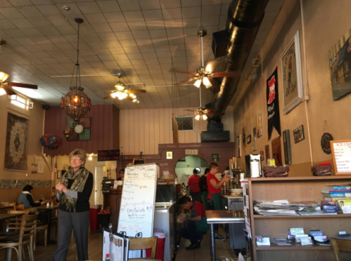 A cozy café interior with patrons, staff, and decorative elements like fans and artwork on the walls.