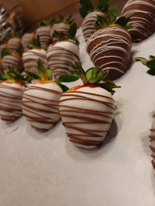 A close-up of chocolate-covered strawberries drizzled with white and dark chocolate, arranged on parchment paper.
