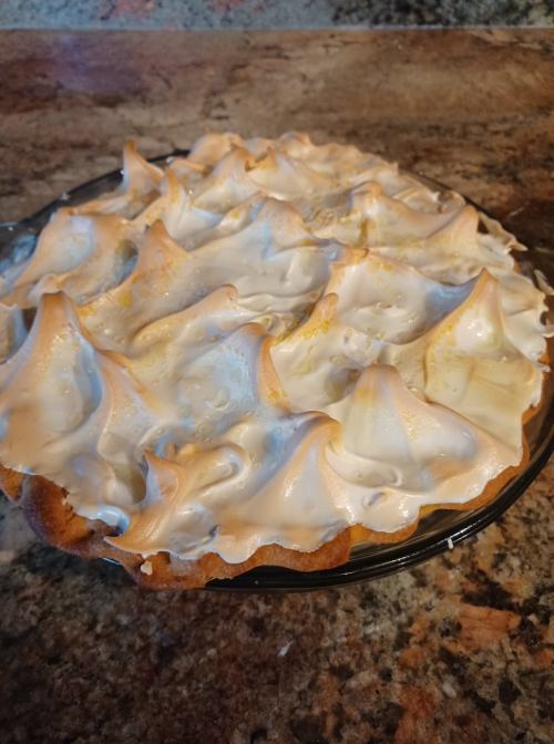 A freshly baked pie with a golden, fluffy meringue topping on a marble countertop.