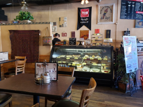 Cozy café interior with a display case of desserts, wooden tables, and a menu board on the wall.