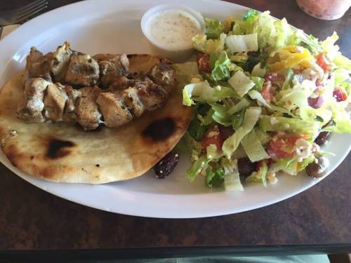 Grilled chicken skewers on flatbread with a side salad of lettuce, tomatoes, and dressing.
