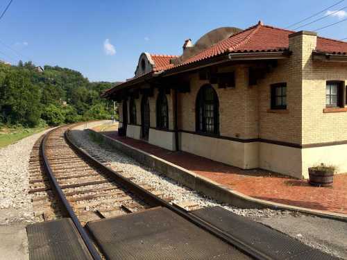 Historic train station with a curved track, surrounded by greenery and a clear blue sky.