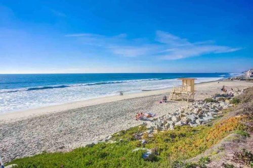A sunny beach scene with gentle waves, a lifeguard tower, and people relaxing on the sand.