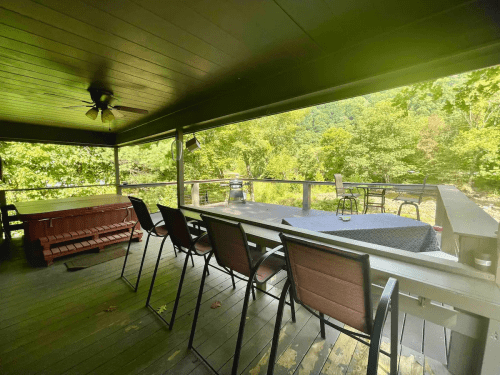 A covered porch with a dining table and chairs, overlooking a scenic view of trees and mountains.