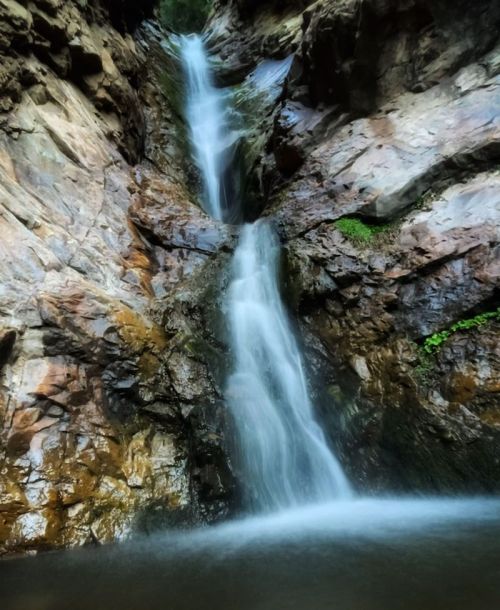 A serene waterfall cascading down rocky cliffs, surrounded by lush greenery and a tranquil pool at the base.