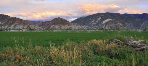 Lush green fields in the foreground with rolling mountains and a colorful sky at sunset in the background.