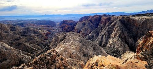 A panoramic view of rugged mountains and valleys under a cloudy sky, showcasing natural rock formations and distant peaks.