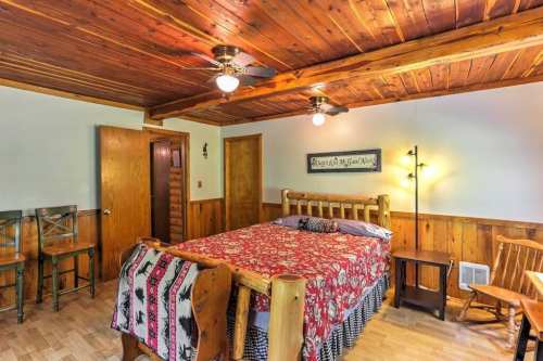 Cozy bedroom with wooden ceiling, a large bed, and rustic decor, featuring a chair and small bar area.