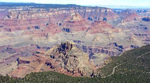 A panoramic view of the Grand Canyon, showcasing layered red rock formations and rugged terrain under a clear blue sky.