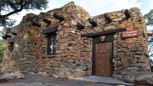 Exterior of the Tusayan Museum, featuring a stone building with wooden beams and a sign above the entrance.