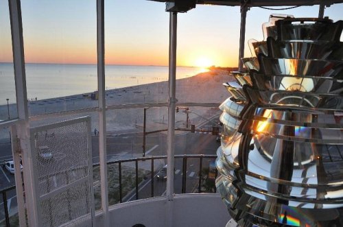 View from a lighthouse at sunset, showcasing the beach and ocean with a lens in the foreground.