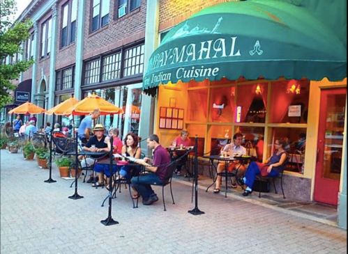 Outdoor dining scene at an Indian restaurant, with patrons enjoying meals under orange umbrellas.