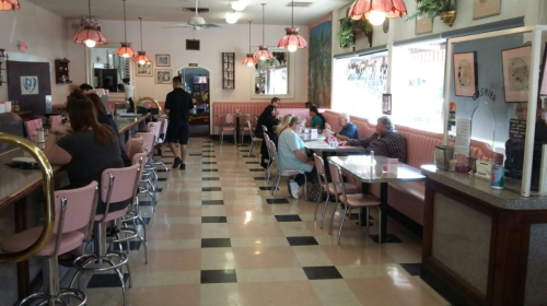 A retro diner with pink booths and chrome accents, featuring customers dining and a waitress serving.