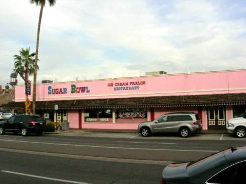 A pink building with "Sugar Bowl Ice Cream Parlor Restaurant" signage, surrounded by palm trees and parked cars.