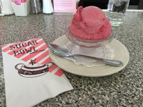 A bowl of pink ice cream on a lace doily, with a spoon and a menu featuring a vintage design.