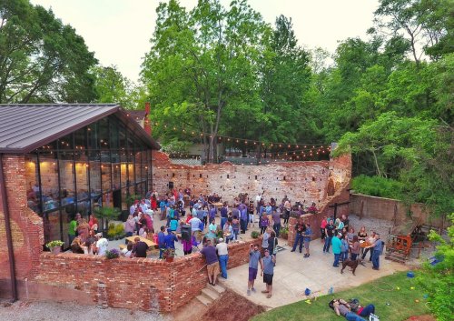 A lively outdoor gathering at a rustic venue, with people socializing and enjoying the greenery around them.