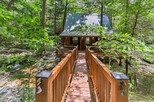 A wooden bridge leads to a cozy cabin surrounded by lush greenery and trees.