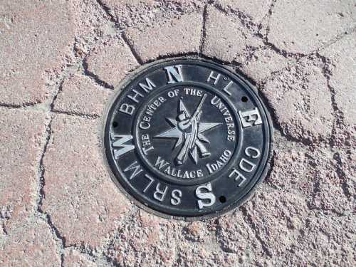 A metal marker on the ground labeled "The Center of the Universe" in Wallace, Idaho, with directional letters and a star design.