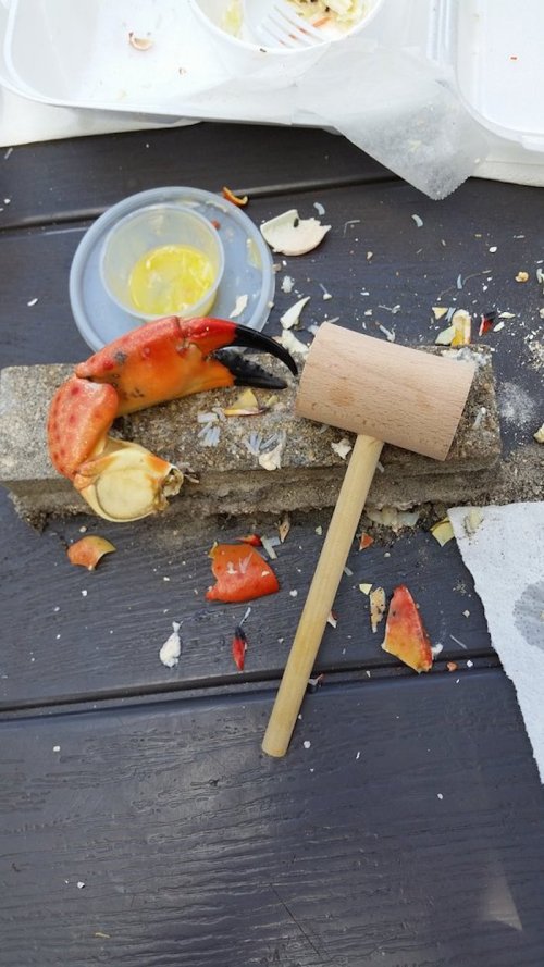 A wooden mallet rests beside a crab claw on a table scattered with crab shells and a small container of dipping sauce.
