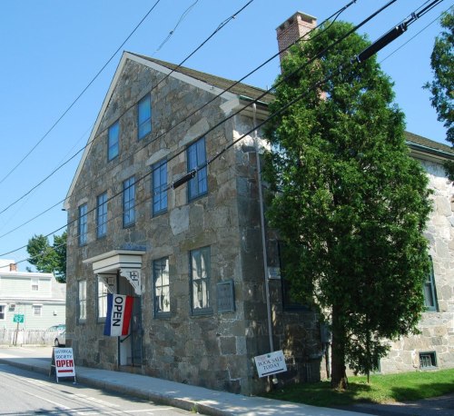 A stone building with a "OPEN" sign and a large tree in front, set against a clear blue sky.
