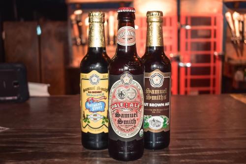 Three bottles of Samuel Smith beer: Oatmeal Stout, Pale Ale, and Nut Brown Ale, displayed on a wooden table.