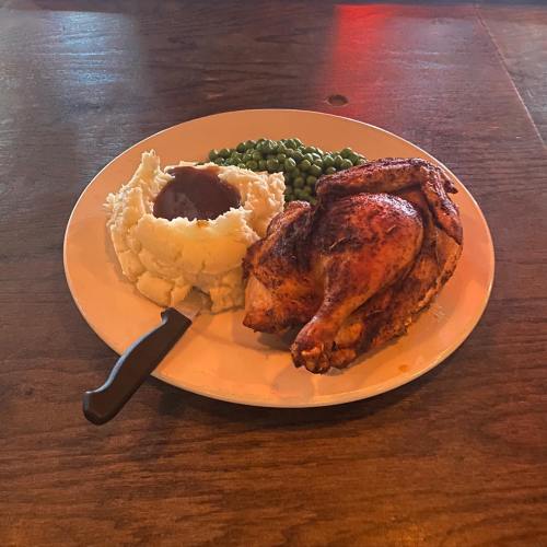 A plate with roasted chicken, mashed potatoes with gravy, and green peas on a wooden table.