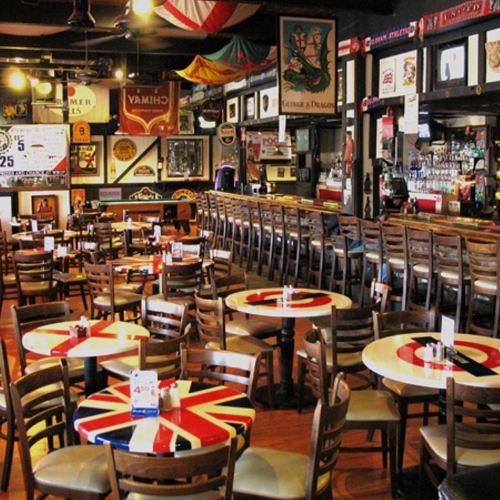 A cozy pub interior with wooden tables featuring Union Jack designs, a long bar, and vintage decor on the walls.