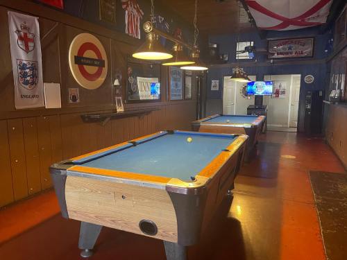 Two pool tables in a cozy bar, decorated with flags and memorabilia, with a TV visible in the background.