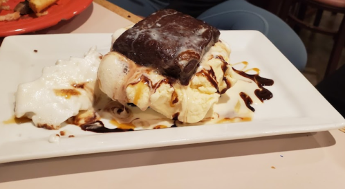 A dessert plate featuring a brownie on top of vanilla ice cream, drizzled with chocolate sauce and whipped cream.