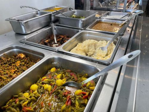 A buffet-style serving area with various trays of colorful dishes, including vegetables and sauces.