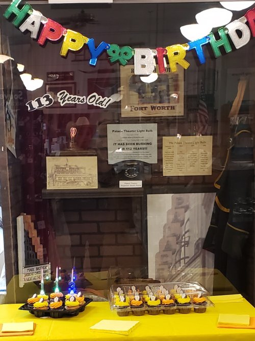 A display celebrating a birthday with a "Happy Birthday" banner, cupcakes, and historical artifacts in a glass case.