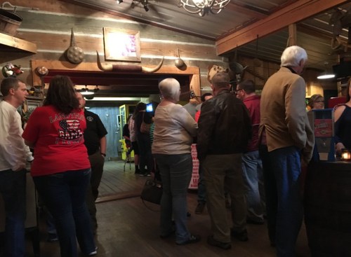 A crowded rustic restaurant interior with people chatting and enjoying the atmosphere.