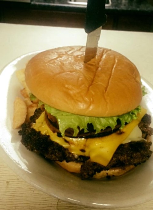 A large burger with lettuce, cheese, and a knife stuck in the top, served with fries on a plate.