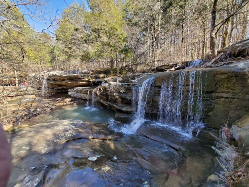 A serene waterfall cascading over rocky ledges, surrounded by trees in a peaceful forest setting.