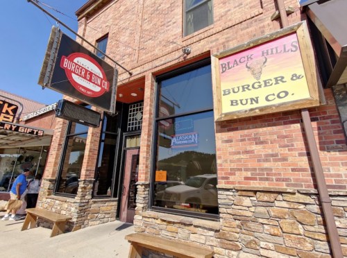 Exterior of Burger & Bun Co. with brick facade and signage, located in a bustling area with pedestrians nearby.