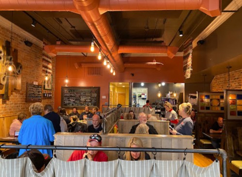 A busy restaurant interior with patrons seated in booths, exposed brick walls, and warm lighting.