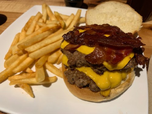 A double cheeseburger with bacon on a bun, served with a side of golden French fries.